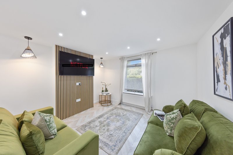 Bright living room with two green sofas, wooden storage unit, window and framed artwork