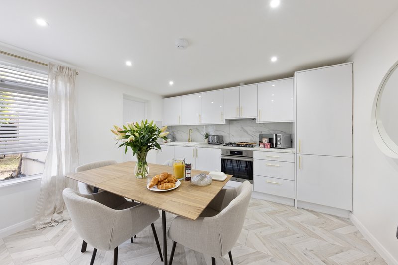 Modern white kitchen with wooden dining table, two chairs, flowers and fruit bowl