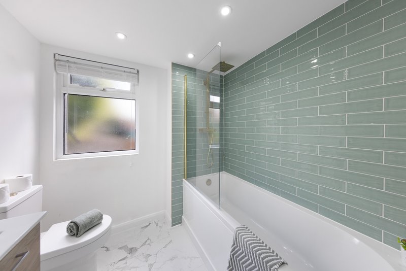 Modern bathroom with white vanity, marble floor, green subway tile wall and soaking tub