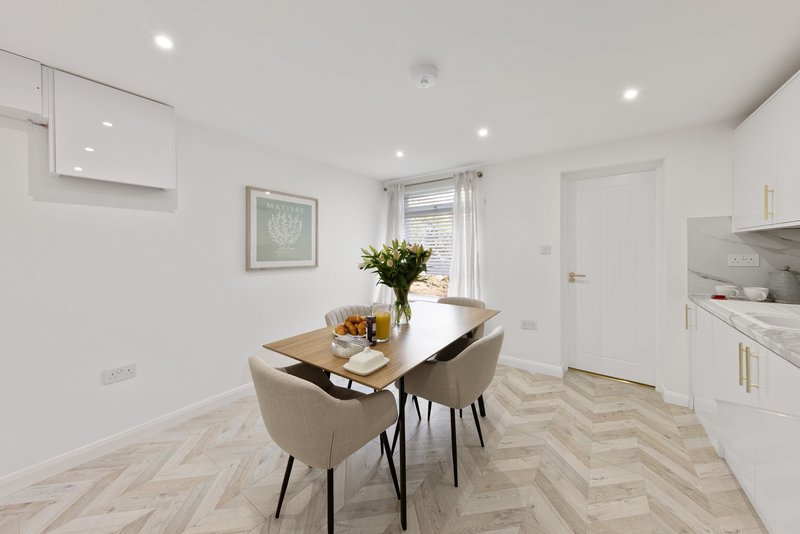 Modern kitchen-diner with dining table, two chairs, white cabinetry and herringbone flooring