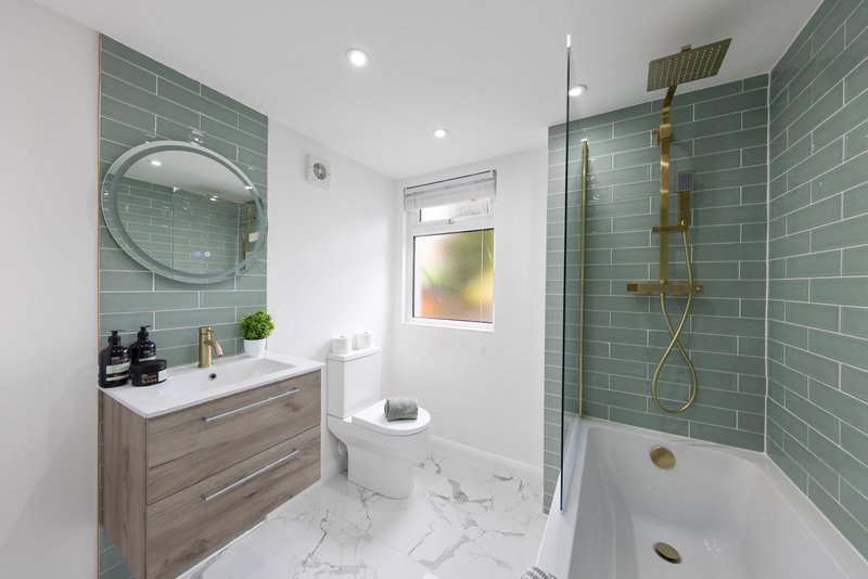 Modern bathroom with green subway tile, marble floor, wooden vanity and round mirror