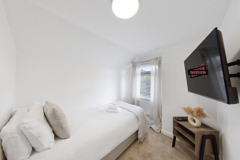 Small bright bedroom with single bed, white bedding, wall-mounted TV and wooden side table