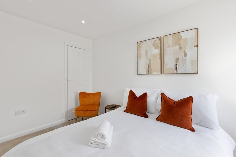 Modern bedroom with white bed, rust and burgundy cushions, wooden chair, framed wall art