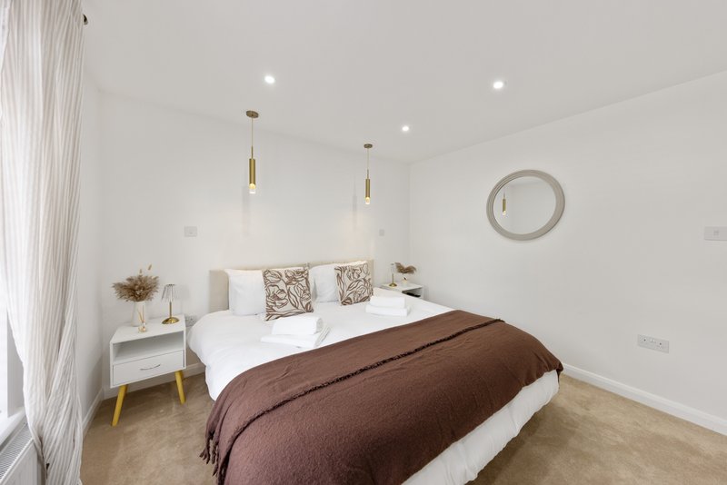 Modern bedroom with double bed, brown throw, white bedding, pendant lights and round mirror