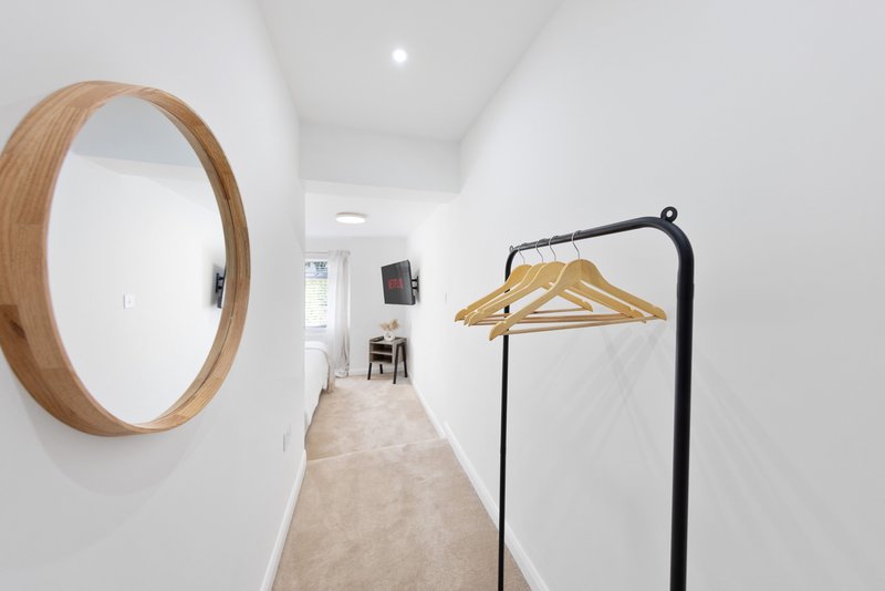 Minimalist hallway with round wooden mirror, clothing rail with hangers, and recessed lighting