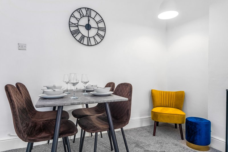 Modern dining area with table, brown chairs, wall clock, and yellow accent chair