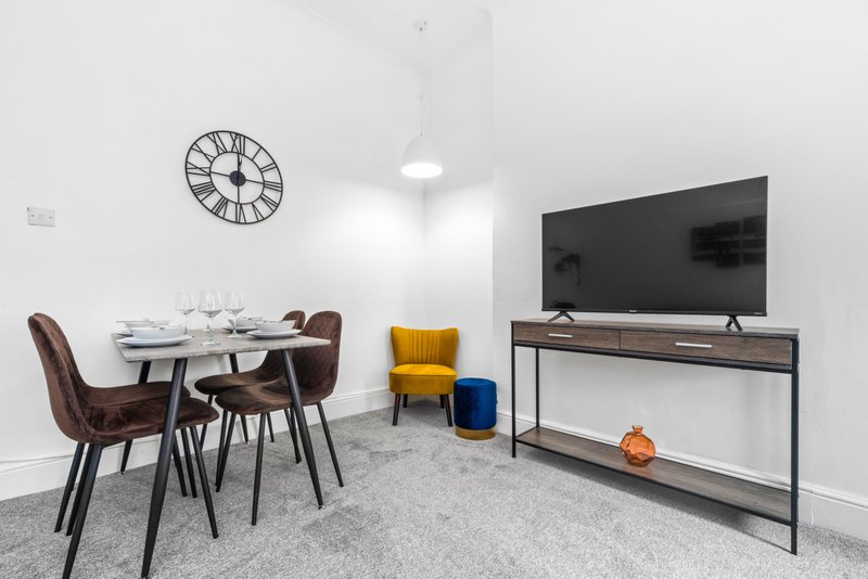 Modern open-plan living space with dining table, chairs, TV, and yellow accent chair