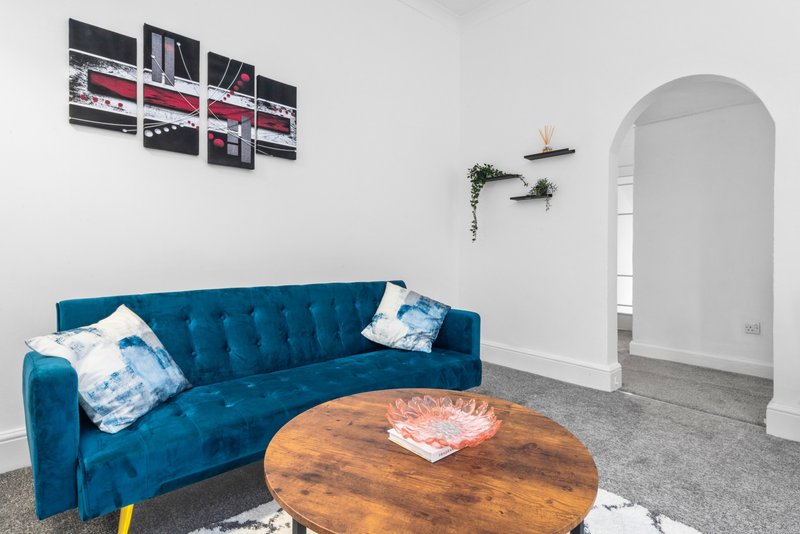 Living room with blue velvet sofa, wooden round table, wall art, and arched doorway