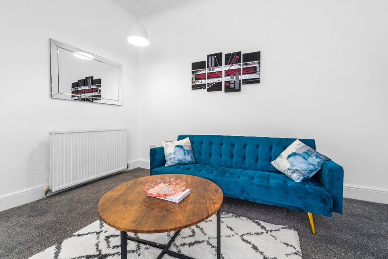 Living room with blue velvet sofa, wooden round coffee table, gray carpet, and wall art