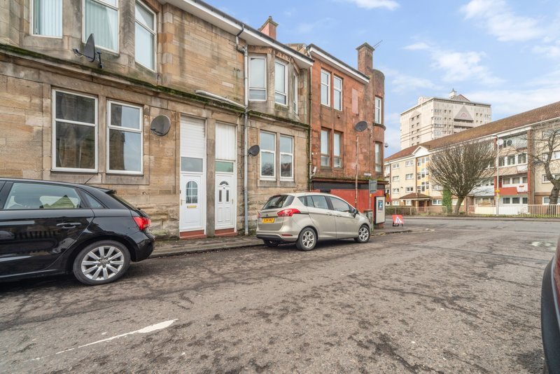 Terraced brick building with red door, street frontage, parked cars and urban square
