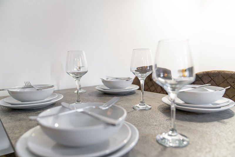 Dining table set with white plates, wine glasses, and cutlery for multiple place settings