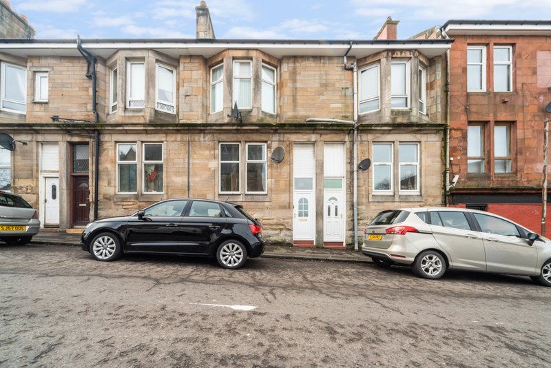 Stone tenement building exterior with parked cars and driveways in front