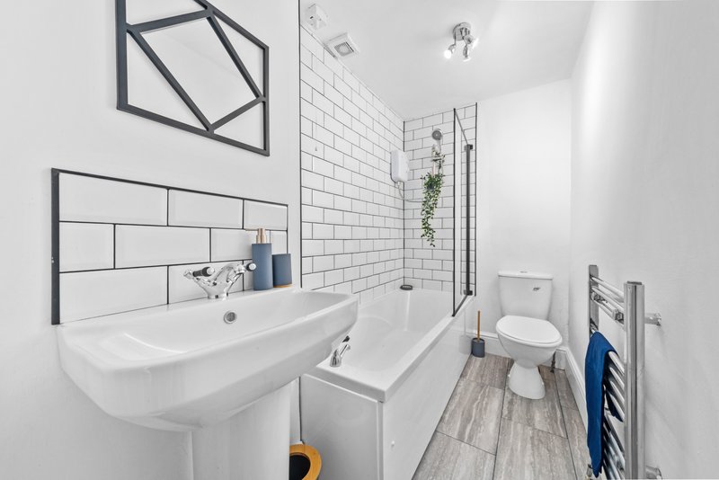 Modern bathroom with white subway tiles, pedestal sink, bathtub, toilet and heated towel rail