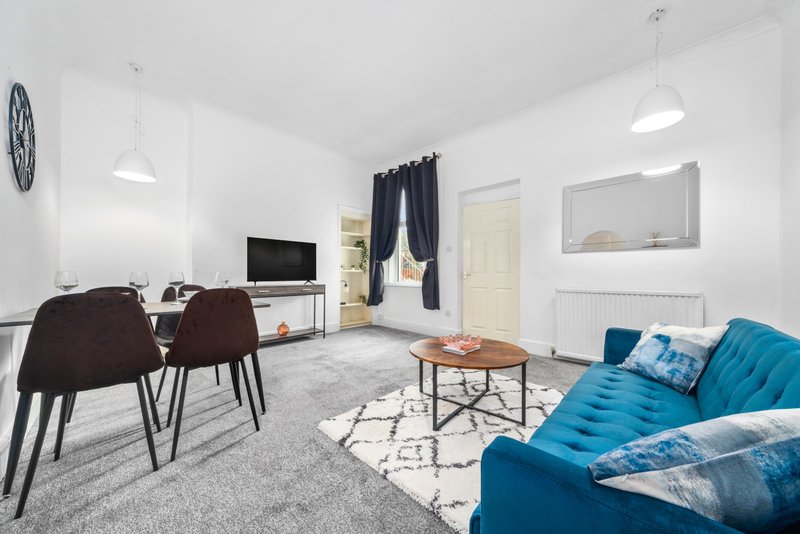 Open-plan living room with blue sofa, dining area, TV, and modern furnishings