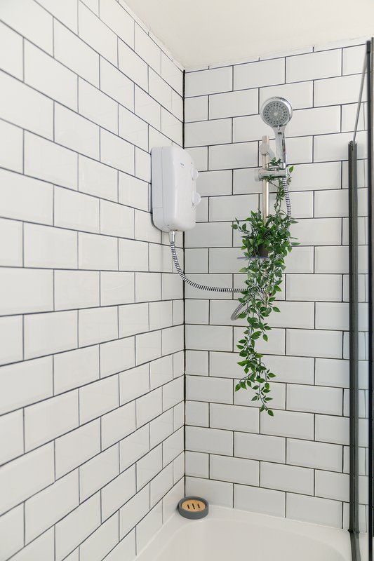 Shower cubicle with white subway tile walls, rainfall showerhead, and trailing green plant