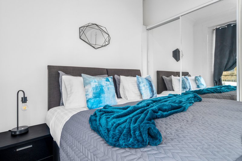 Modern bedroom with double bed, blue throw blanket, white pillows and dark headboard