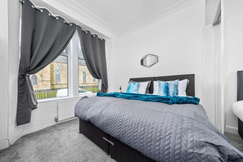 Bright bedroom with double bed, gray bedding, blue cushions, gray curtains and bay window
