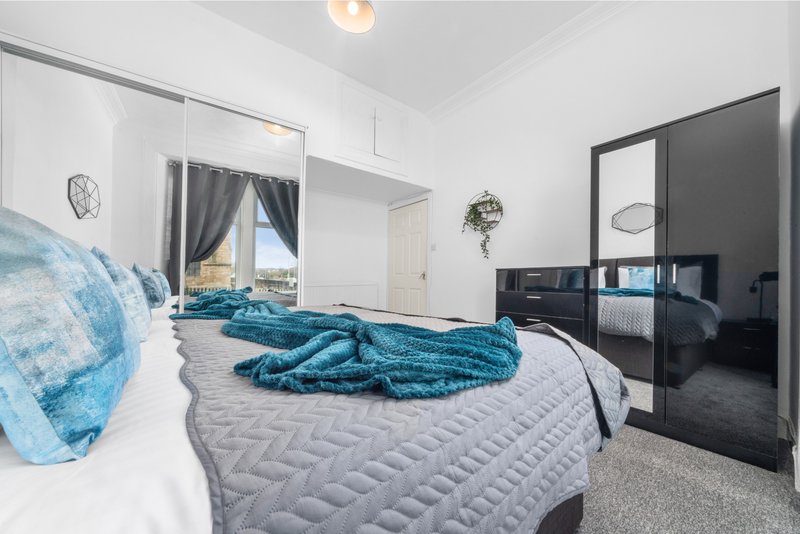 Bright bedroom with double bed, turquoise bedding, mirror wardrobe and ensuite bathroom visible