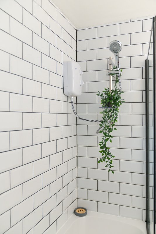 Modern bathroom shower corner with white subway tiles, showerhead, and hanging trailing plant