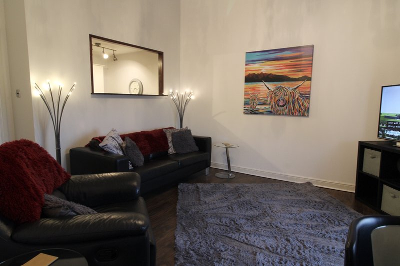 Living room with black leather sofas, floor lamps, wall art, and television setup
