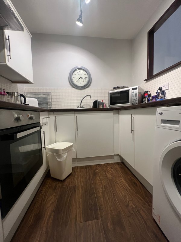 Modern kitchen with white cabinetry, wood-effect flooring, integrated appliances and wall clock