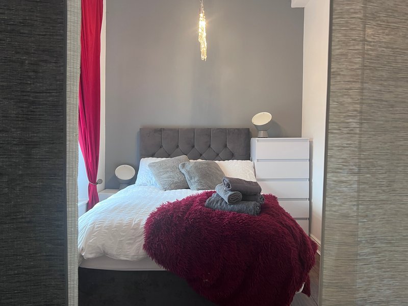 Modern bedroom with gray upholstered bed, white bedding, burgundy throw blanket and decorative pillows