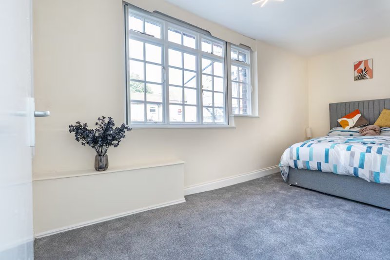 Bright bedroom with double bed, grey carpet, large window and vase of flowers
