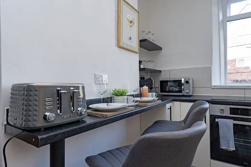 Modern kitchen with black countertop, gray toaster, microwave, and workspace with chair