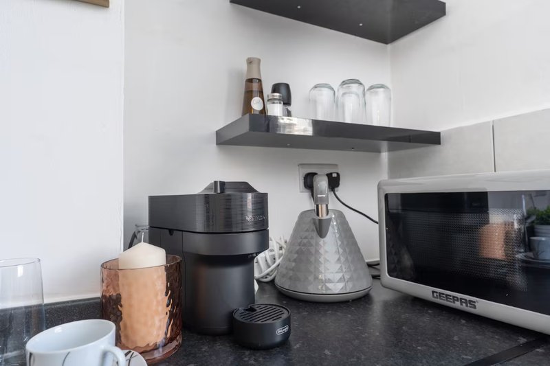 Modern kitchen counter with coffee maker, microwave, and organized shelf with glassware
