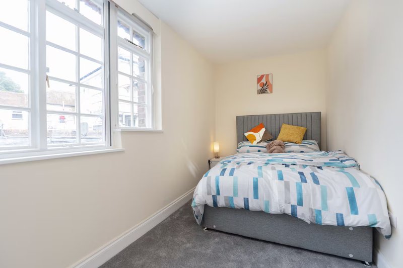 Bright bedroom with double bed, grey headboard, striped duvet, and large window