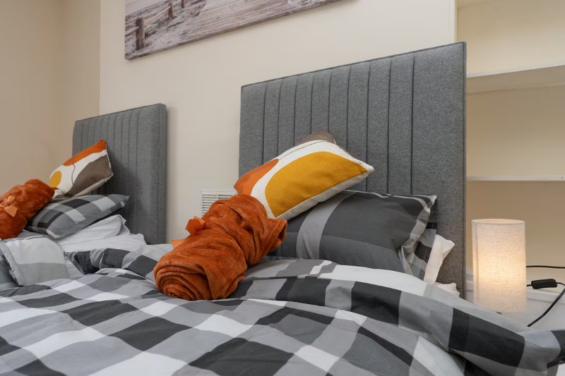 Modern bedroom with two gray upholstered headboards, checkered bedding, and decorative pillows