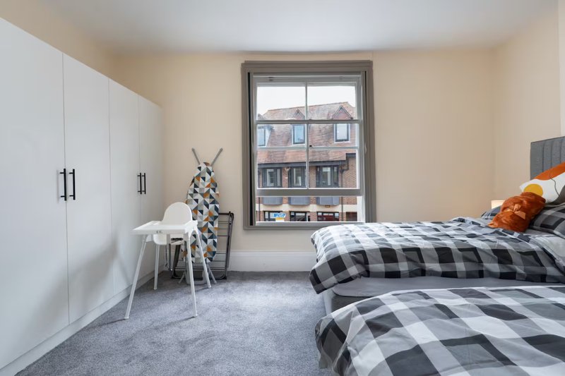 Bright bedroom with twin beds, white wardrobe, small table and window overlooking street