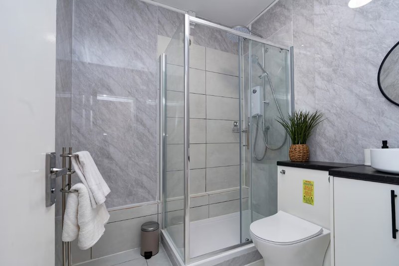 Modern bathroom with walk-in shower, toilet, sink, and marble-effect tiling