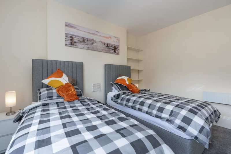 Twin bedroom with checkered bedding, gray headboards, orange pillows and wall art