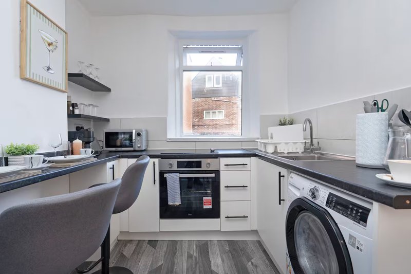 Modern kitchen with white cabinets, black countertops, integrated appliances and washing machine