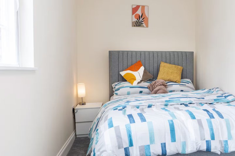 Bedroom with gray upholstered headboard, blue and white patterned bedding, cushions, and bedside lamp