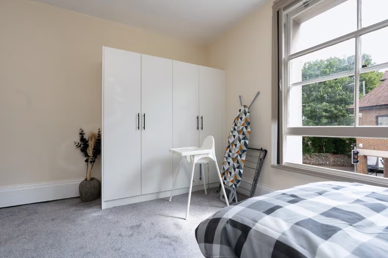 Bright bedroom with white wardrobe, desk, single bed and large window overlooking garden