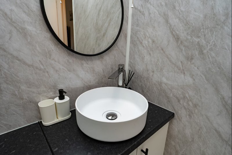 Modern bathroom with round white sink, black countertop, circular mirror and toiletries
