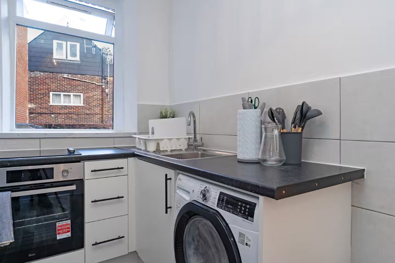 Modern kitchen with white cabinetry, black countertop, integrated washing machine and oven