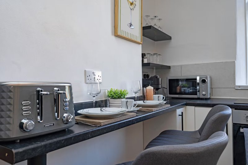 Modern kitchen with black countertop, grey toaster, microwave, and dining chair
