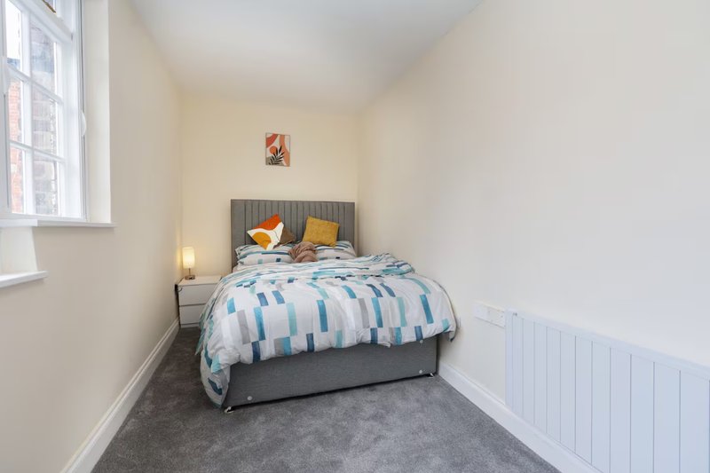 Small bedroom with double bed, grey headboard, striped bedding and yellow cushions