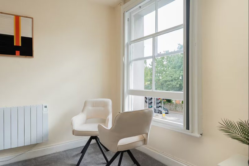 Bright modern room with two cream chairs, large window overlooking garden, radiator and abstract wall art