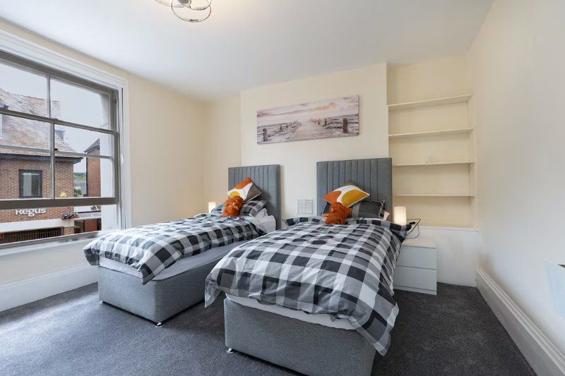 Bright bedroom with two single beds, checkered bedding, built-in shelving and window view