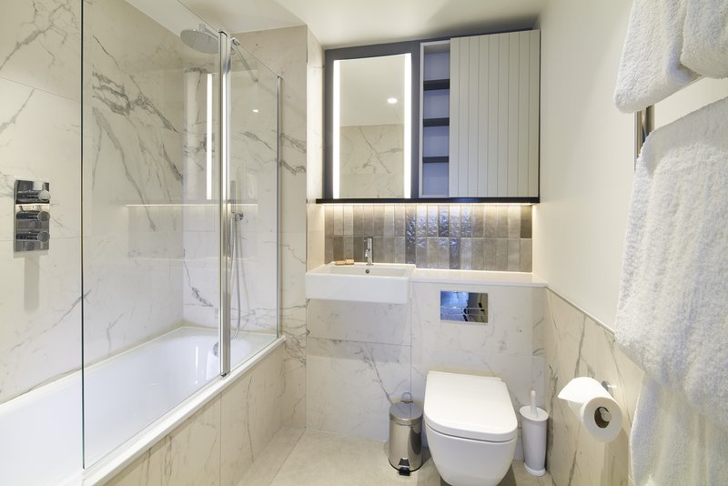 Modern bathroom with marble shower enclosure, white toilet, sink and mirror cabinet
