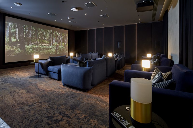 Modern home theater room with dark seating, projection screen showing forest scene, and ambient lighting