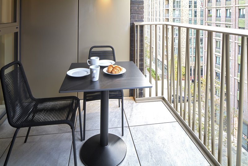 Balcony with small dining table, chairs, place settings and city view