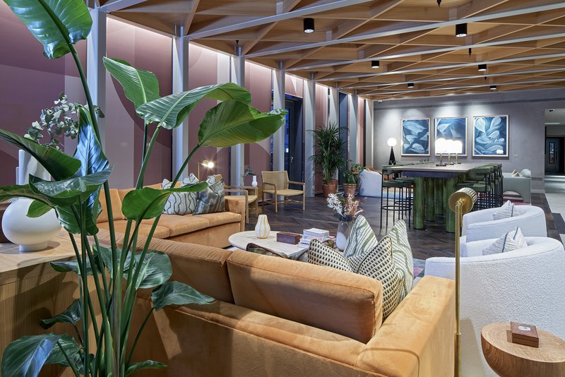 Modern open-plan living area with tan leather sofas, potted plants, wooden ceiling beams and framed artwork