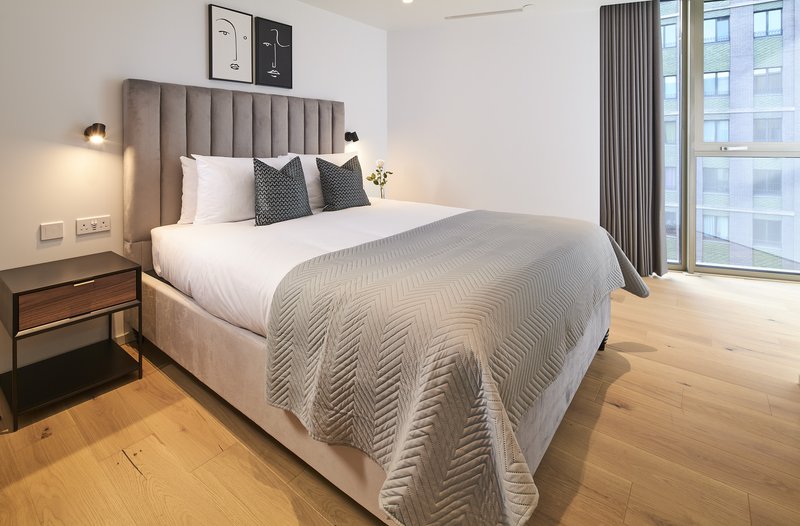 Modern bedroom with upholstered headboard, white bedding, wooden flooring and floor-to-ceiling windows