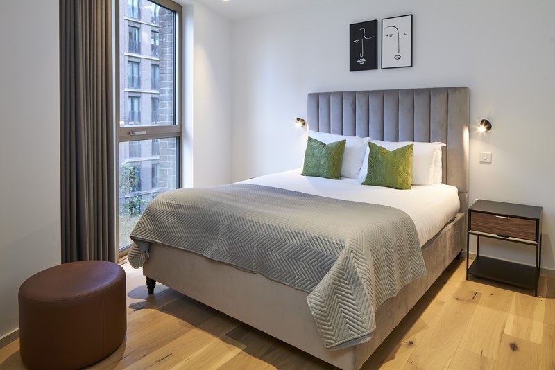 Modern bedroom with upholstered bed, wooden nightstand, green cushions, and city window view
