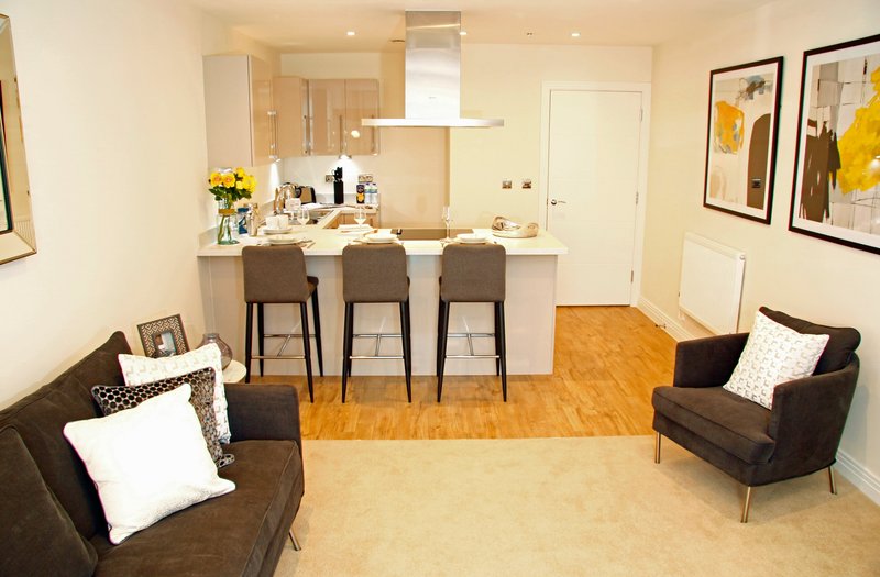 Open-plan living and kitchen area with brown seating, bar stools, and framed wall art